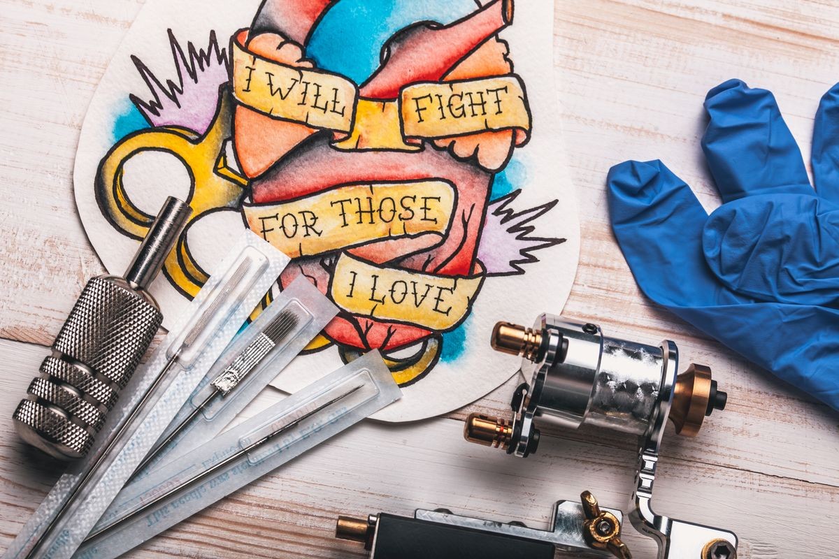 Replacement supplies for tattoo in sterile packages, sketches, inks and a tattoo machine on the white background of old boards Replacement supplies for tattoo in sterile packages, sketches, inks and a tattoo machine on the white background of old boards